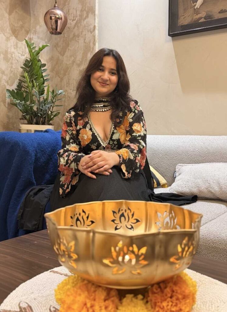 Neelam wearing the Perfect ethnic wear Alaya Noor Signature Black Floral Anarkali with Choker Dupatta, sitting gracefully with a golden bowl decor in a festive setting.